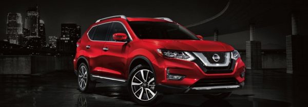 Red 2019 Nissan Rogue in the foreground of a city skyline at night